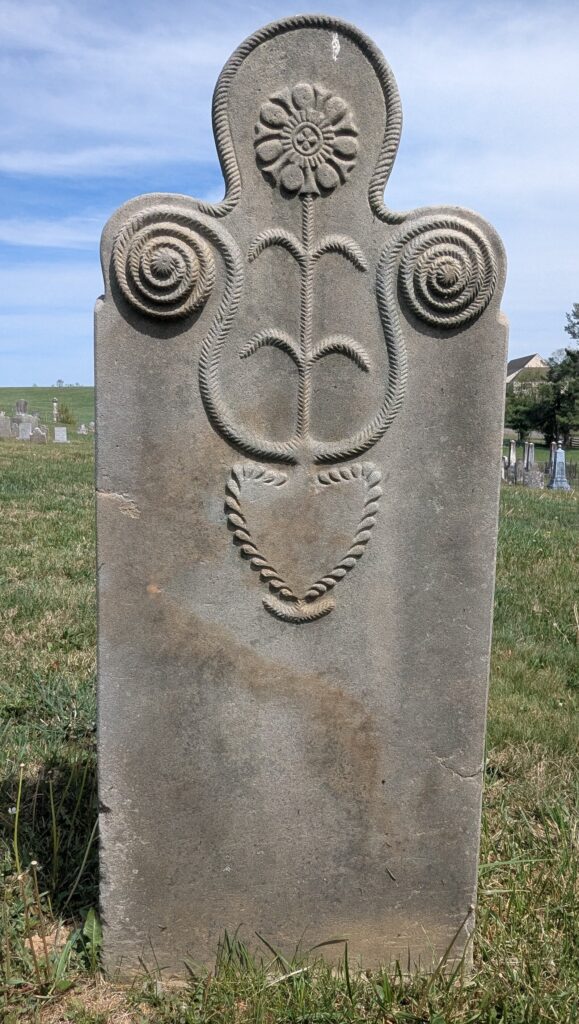 Repass headstone carved by Krone with a central rosette, spiral shoulders, lily stem, and roped heart at base